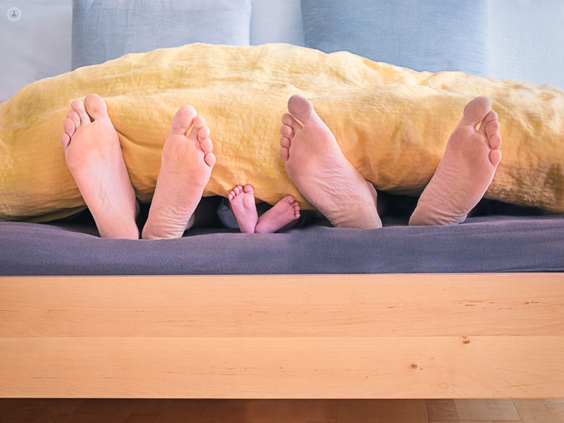 piedi di una coppia di genitori e di suo figlio che escono dalla coperta di un letto