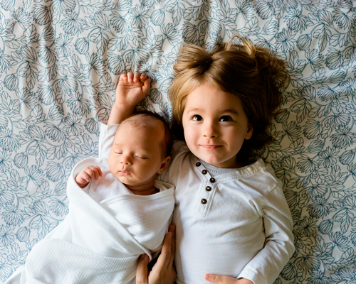 una bambina e un neonato stesi sul letto