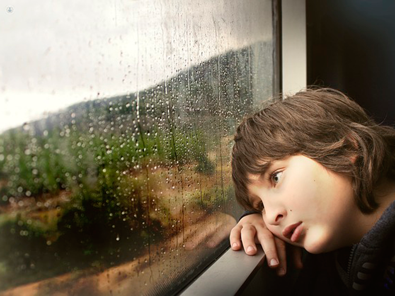 bimbo triste che guarda fuori dalla finestra mentre piove