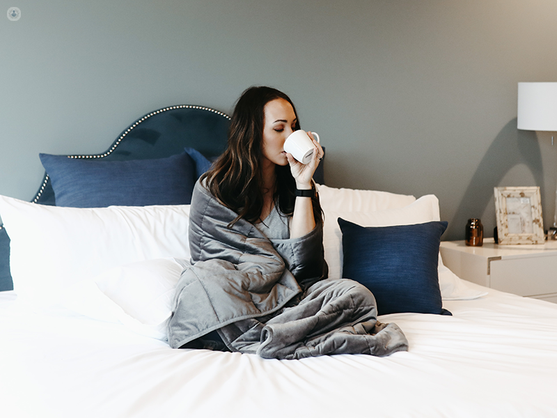 ragazza sul letto con una coperta che beve un tè